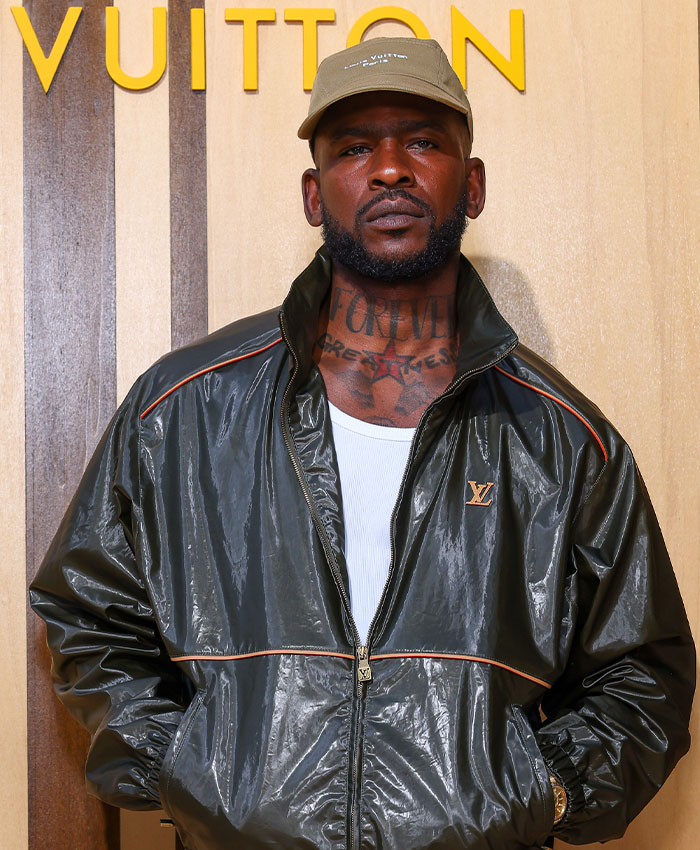 Man in a green cap and jacket with neck tattoos, captured in a candid moment at an event to protect your kids.