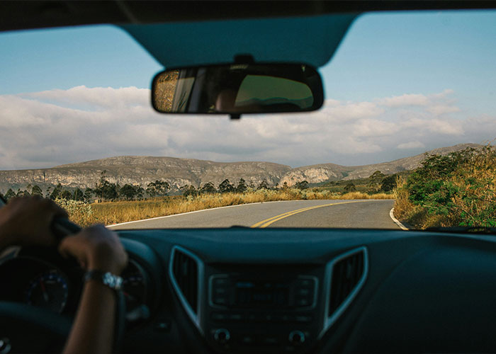View of winding country road from inside car with driver holding steering wheel View of winding country road from inside car with driver holding steering wheel
