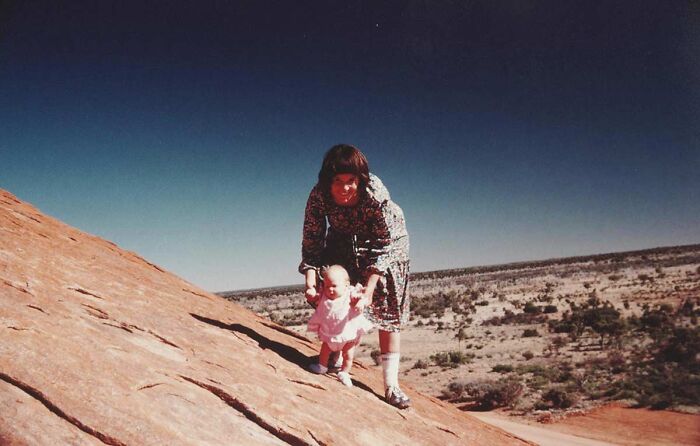 Woman helping toddler walk on large rock in desert landscape