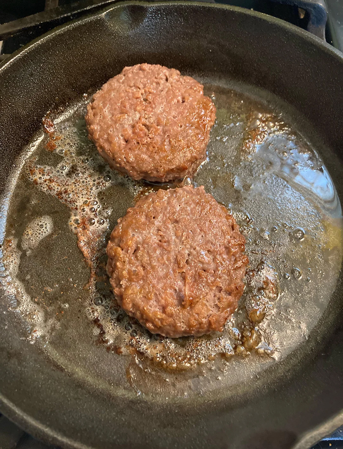 Two burger patties cooking in a pan representing cooking myths about burger preparation