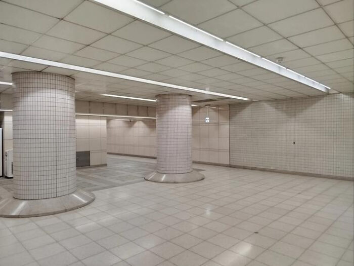 An expansive, empty subway station platform with tiled walls and columns, an example of a haunting liminal space.