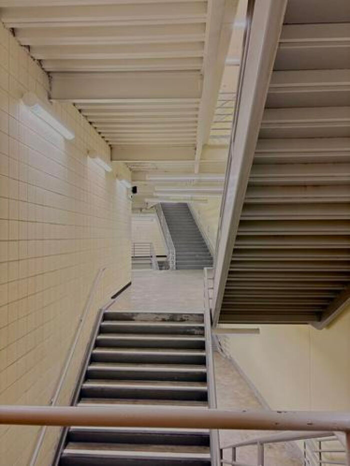 A stark, empty stairwell in a building, evoking a haunting liminal space with its repetitive design and muted colors.