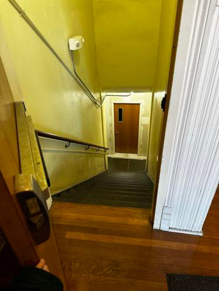 A narrow, yellow-painted stairwell leading to a closed door, creating a haunting liminal space.