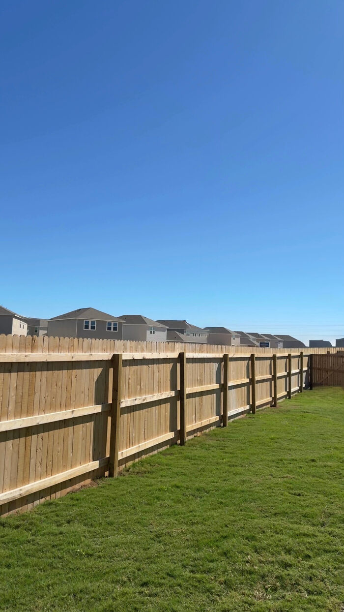 A view of new houses beyond a wooden fence on a sunny day, showcasing a suburban liminal space.