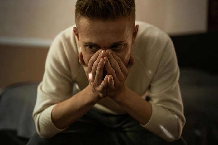 Worried man covering mouth sitting alone in dim room