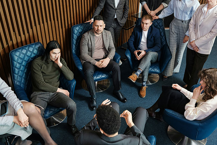 A group of employees gathered in a meeting, with a new hire discussing management's illegal shenanigans.