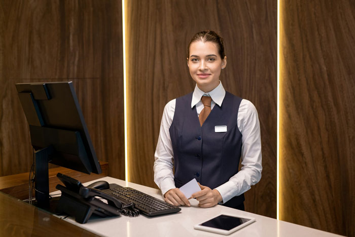 Smiling woman in uniform at a reception desk, reflecting on a job that might be on the line due to her hair.