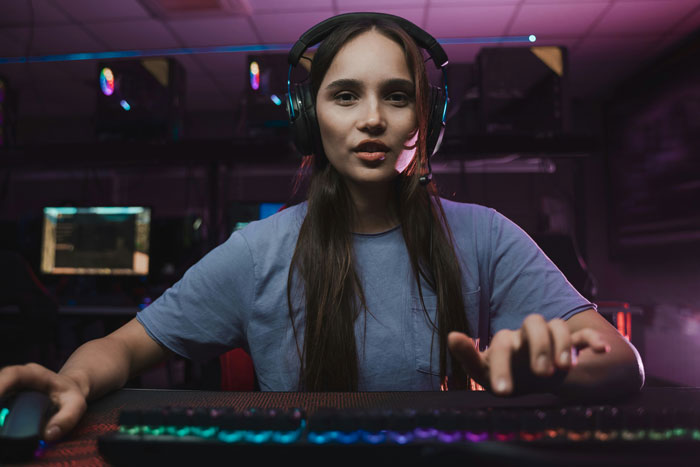 A woman wearing headphones and a microphone, looking directly at the camera while playing a game, highlights her gaming problem.
