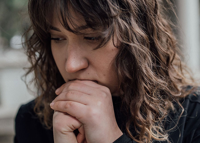 A worried woman with dark curly hair holds her hands to her mouth, contemplating suspicions over her husband. A worried woman with dark curly hair holds her hands to her mouth, contemplating suspicions over her husband.