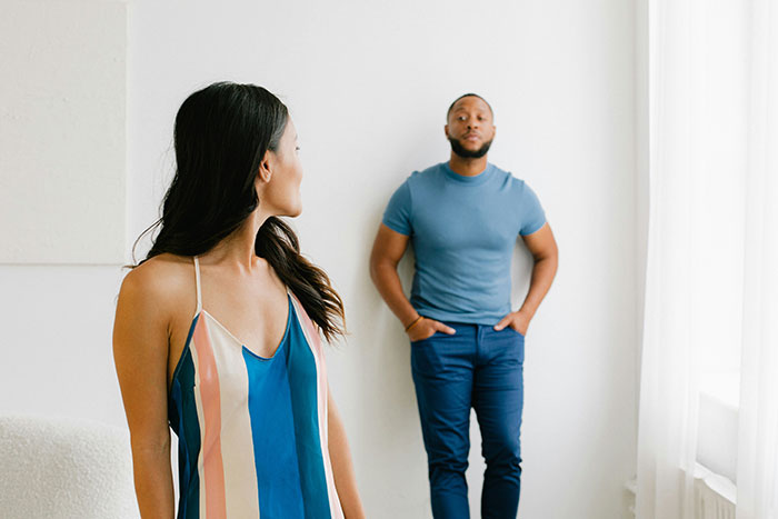 Woman looking at man standing with hands in pockets, depicting tense family relationship Woman looking at man standing with hands in pockets, depicting tense family relationship