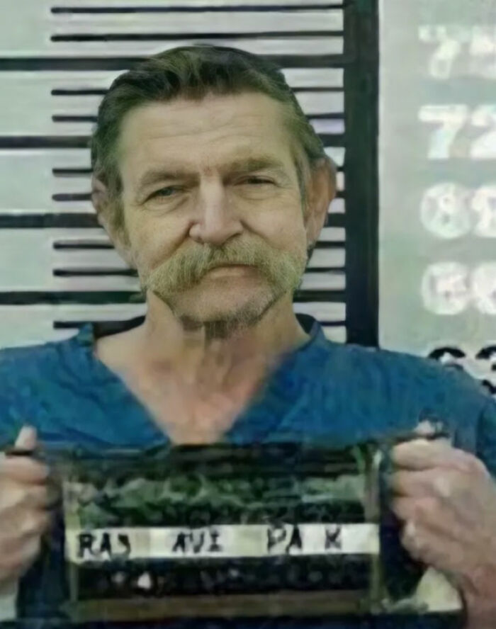 Aging serial killer holding prison placard in a mugshot