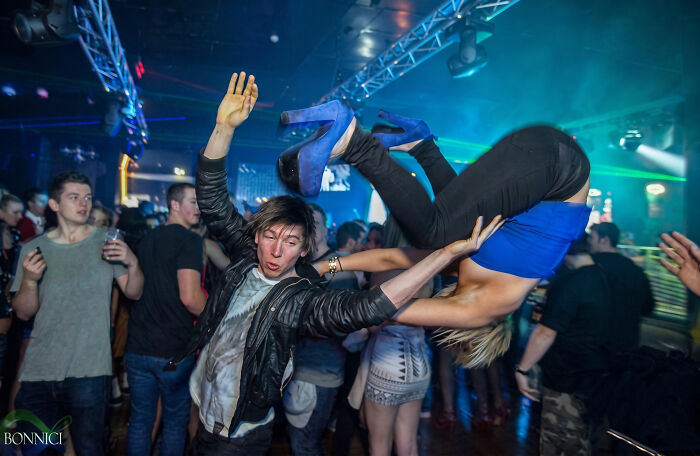 Funny nightclub photo of man flipping woman over in a crowded party scene