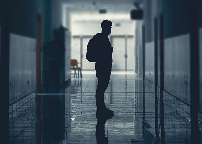 Silhouette of a man standing in a dimly lit hallway with a reflective floor