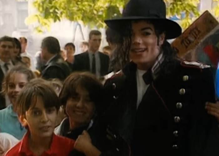 Michael Jackson in signature hat posing with smiling children outdoors