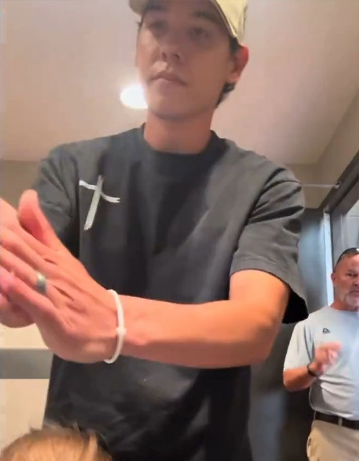 Man in cap standing inside restroom appearing to confront someone with man in background Man in cap standing inside restroom appearing to confront someone with man in background