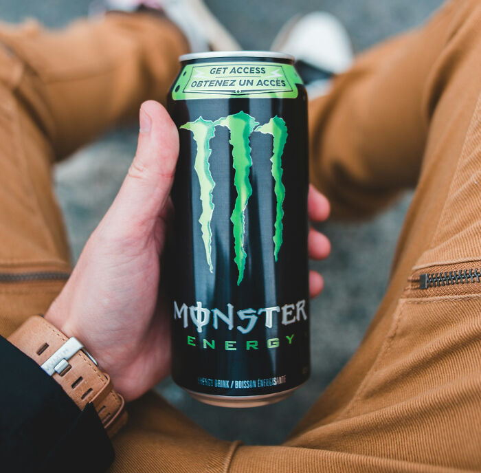 A hand holds a Monster Energy drink can, connecting to health trends and potential intense stress and burnout.