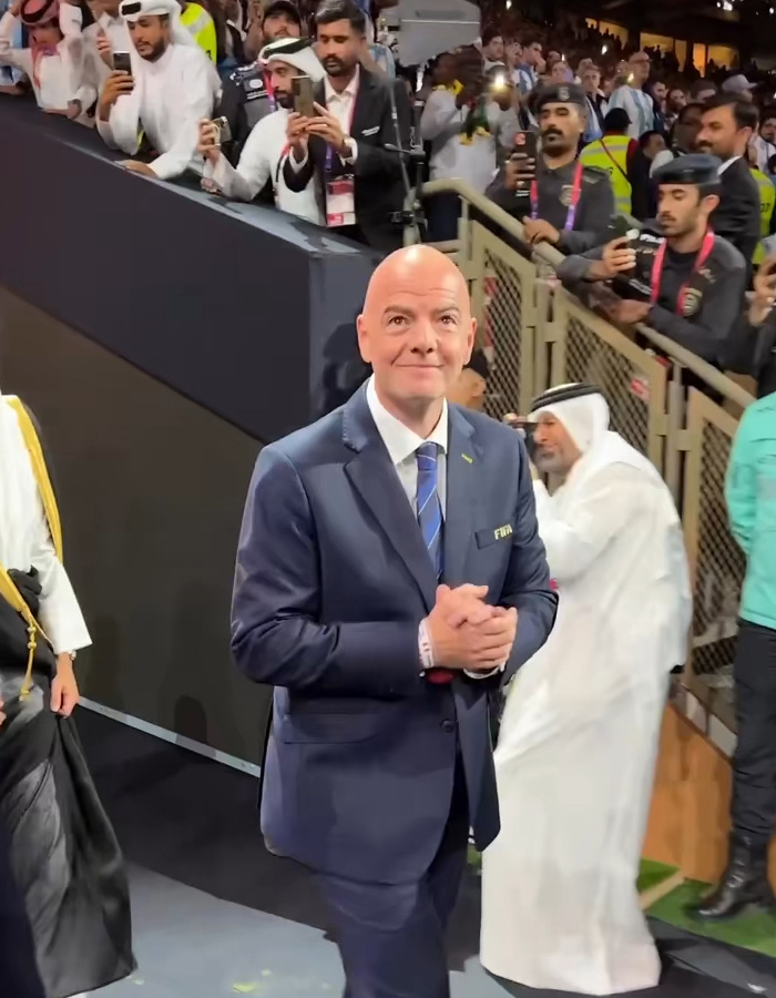 A World Cup boss in a suit smiling at the camera amidst a crowd, hinting at a hypocritical act and soccer scandal. A World Cup boss in a suit smiling at the camera amidst a crowd, hinting at a hypocritical act and soccer scandal.