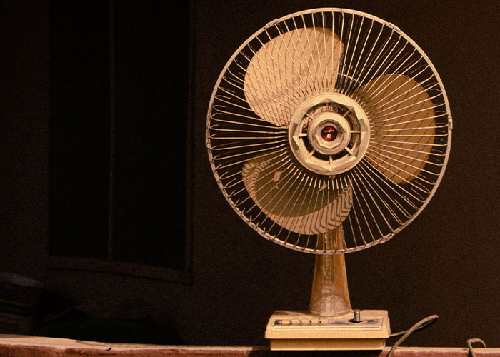 A vintage electric fan, a classic solution to serious problems, standing in a dimly lit room.
