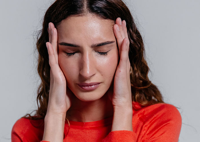 A woman holding her temples, eyes closed, seemingly distressed by horrible things committed by close friends that broke people's trust.