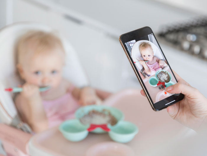 A parent taking a picture of a baby eating, capturing moments that could be heartwarming and heartbreaking on late parents' phones.
