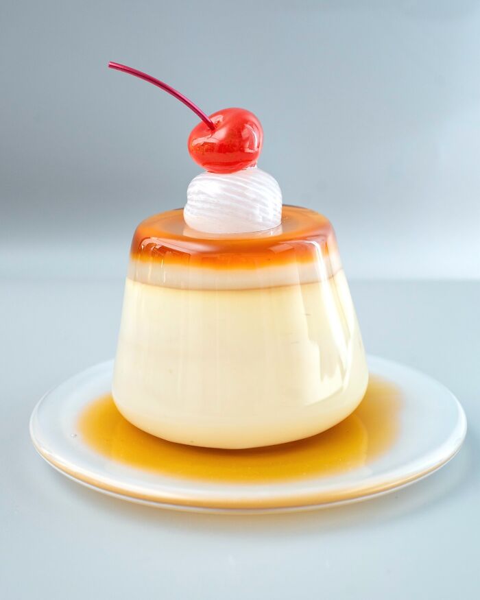 Hyper-realistic glass food pudding with a cherry and whipped cream, an artist's creation that looks good enough to eat.