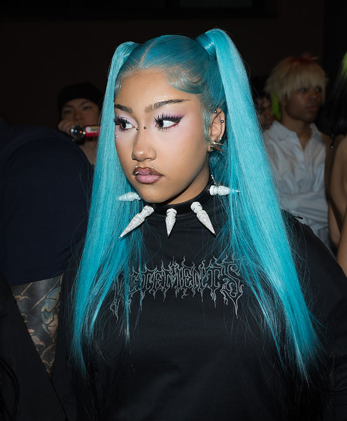 Close-up of North with bright blue hair and a spiked necklace, looking thoughtful, emphasizing the need to protect your kids.