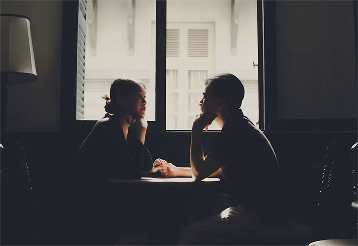 A couple sitting across from each other at a table, with light coming through a window, discussing the husband's memory box and stalkerish tendencies. A couple sitting across from each other at a table, with light coming through a window, discussing the husband's memory box and stalkerish tendencies.