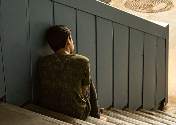 Boy sitting alone on outdoor stairs in solitude, reflecting isolation feeling
