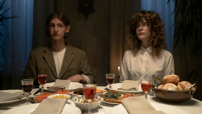 Two people sitting silently at a dining table set for a meal
