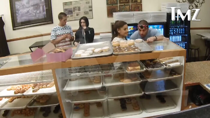 Ariana Grande and friends at a donut shop, looking at the display. This image highlights celebrity scandals and unhinged moments.