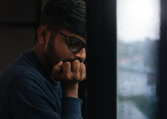 A man looking contemplative by a window, reflecting on advice that is good but socially not acceptable.