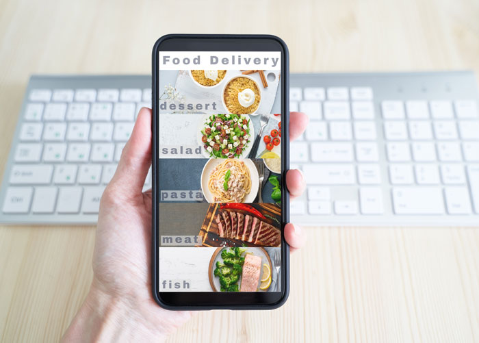 A hand holds a smartphone displaying a food delivery app, showing various meal categories. This image relates to things people saw on their late parents' phones.