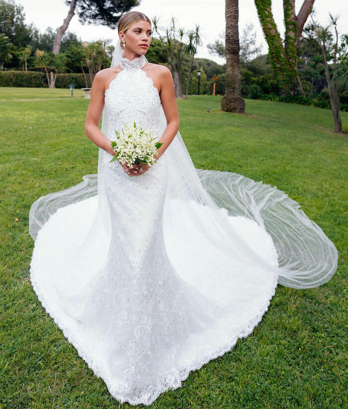 A stunning celebrity wedding dress with a high halter neckline and long train, amidst a lush green garden.