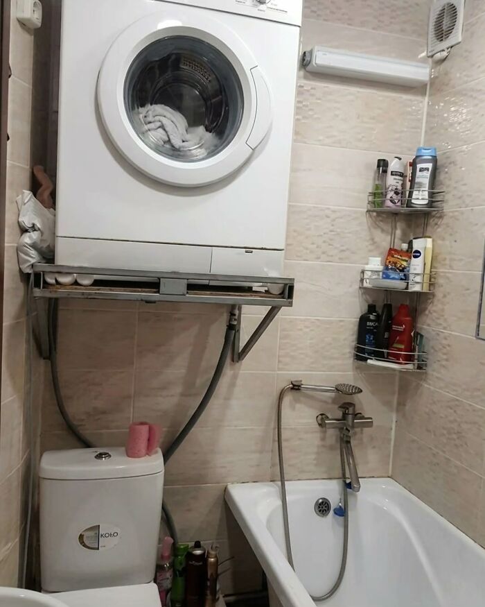 A washing machine precariously installed above a toilet in a small bathroom, an example of Slavic science in action.