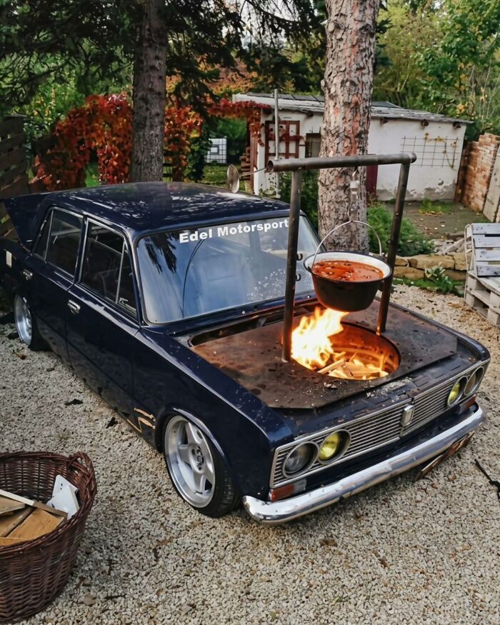 A vintage car with a fire pit and a pot cooking on its hood, demonstrating innovative Slavic Science.