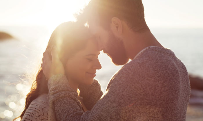 Couple sharing a tender moment in sunlight by the sea Couple sharing a tender moment in sunlight by the sea