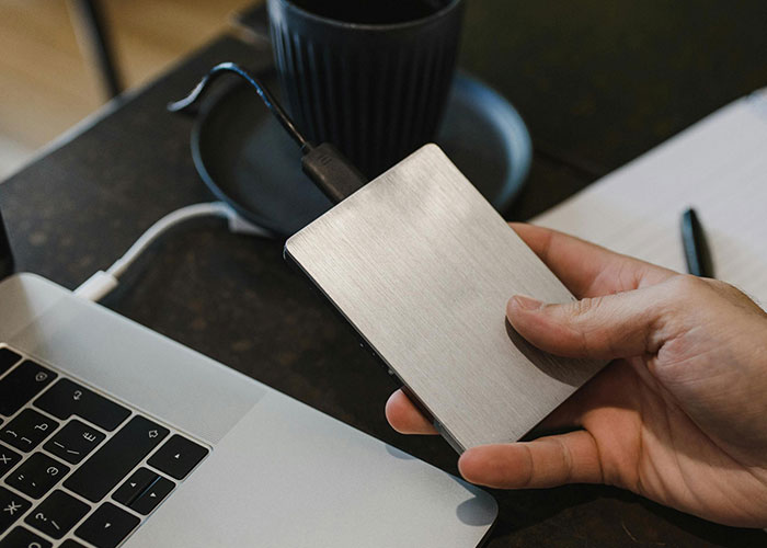 Hand holding external hard drive connected to laptop