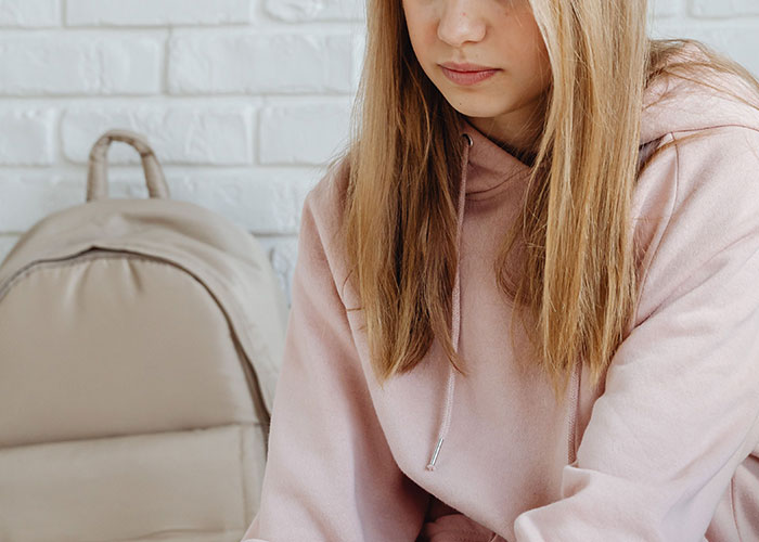 Sad young woman in a pink hoodie sitting indoors looking down, emotional expression