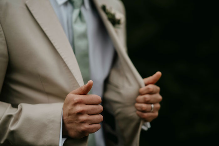 Groom adjusting beige suit jacket at wedding