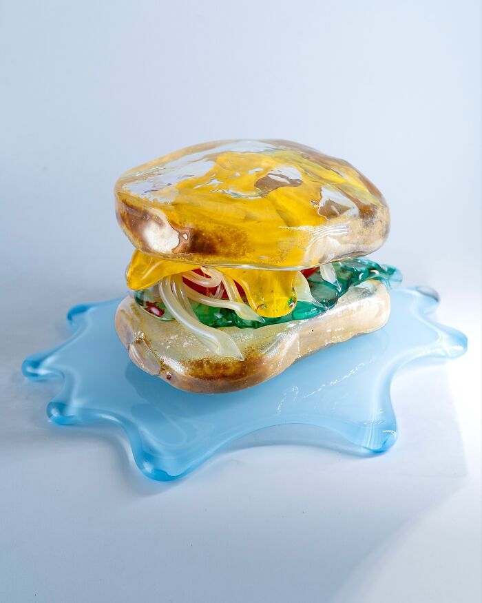 Hyper-realistic glass food burger on a blue glass base, created by a Japanese artist.