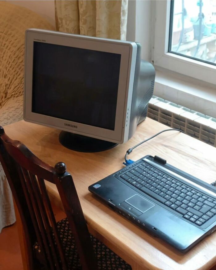 An old CRT computer monitor connected to a laptop on a wooden desk, reflecting Slavic Science ingenuity.