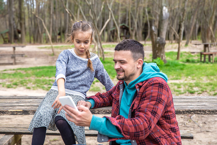 Man showing phone to concerned child outdoors unsettling thing found about friend
