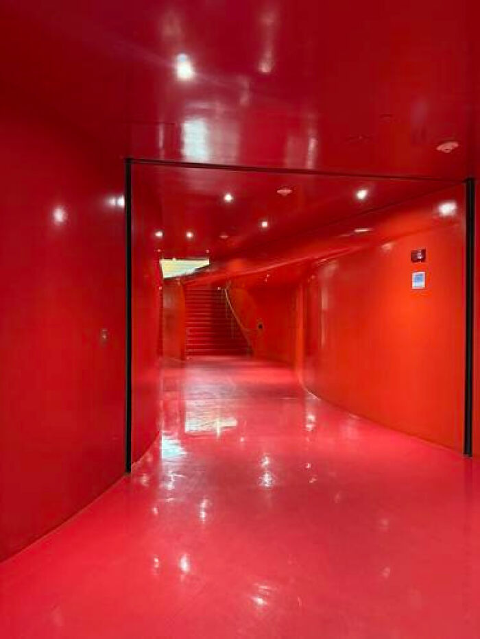 A bright, glossy red hallway with curved walls and a staircase in the distance, a modern liminal space.