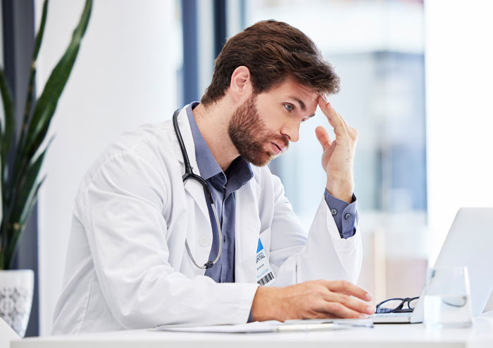 Doctor looking stressed while working at desk in medical office