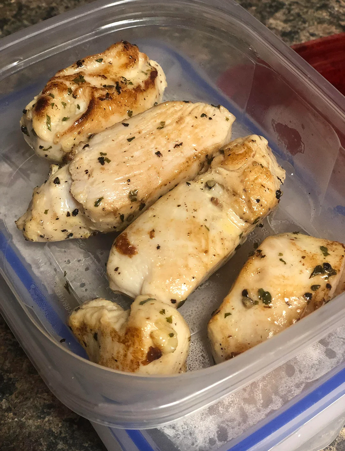 Cooked chicken breasts in a plastic container, addressing cooking myths about reheating and storage