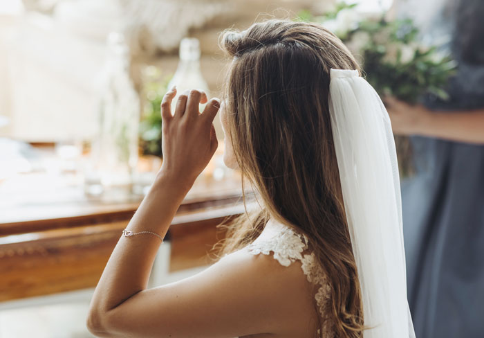Bride touching face with wedding veil and bouquet nearby