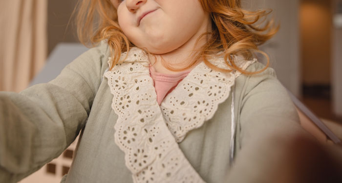 Young girl making face wearing dress with lace collar about body remarks