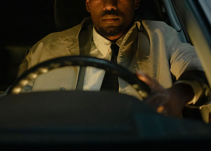 Man in trench coat driving looking serious at night moment to leave immediately