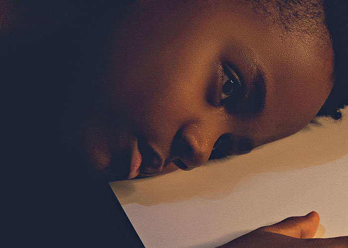 A young person lies on their side, looking towards the viewer, realizing they can't keep contact with their parents.
