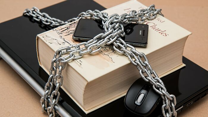 A book, a phone, and a computer mouse are chained to a laptop, symbolizing actions during a date.